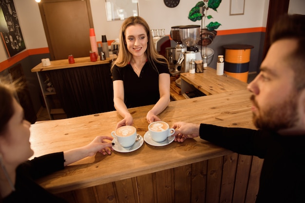 Friendly bartender serving espresso coffee to customers in the interior of a modern coffee shop.