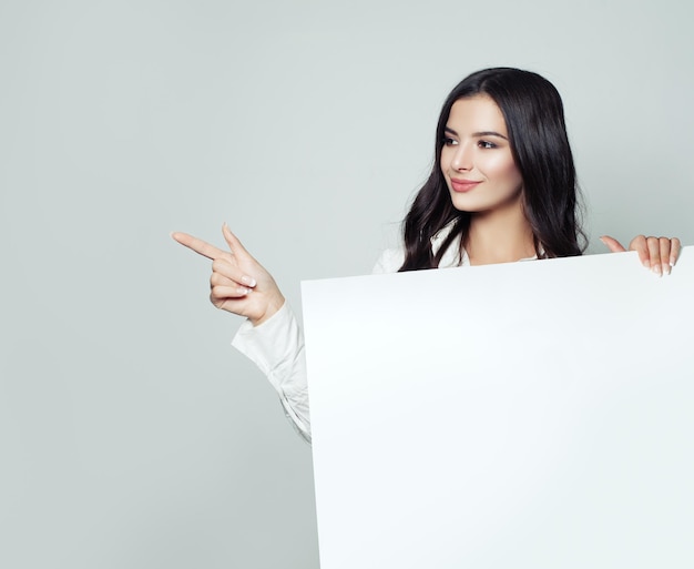 Friendly business woman pointing her finger and showing signboard with blank copy space area for advertisiment or text message on white background