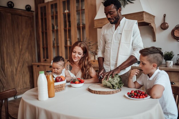 Friendly candid interracial family with two kids spend time together for breakfast at cozy kitchen