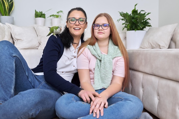 Friendly cheerful family portrait of mom and teenage daughter with green parrot