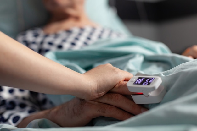 Friendly doctor reassuring sick old patient holding hands