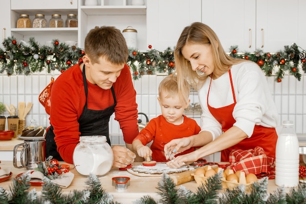 Friendly family making cookies shapes in raw flat dough on a kitchen table using a cookie cutter to make delicious gingerbread cookies to celebrate with family and friends.