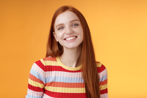 Friendly feminine pretty redhead caucasian female sibling smiling broadly have perfect happy mood talking casually enjoy fine summer sunny day standing orange background delighted relaxed