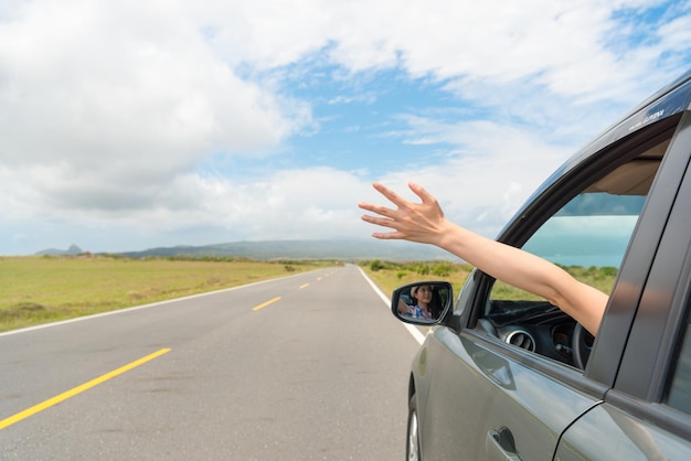 friendly girl sitting on travel car happily reach out hand enjoying own holiday vacation drove stopping on asphalt roadside viewing rural mountain scenery.