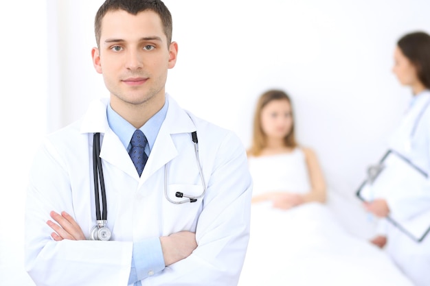 Friendly male doctor on the background with patient in the bed and his physician