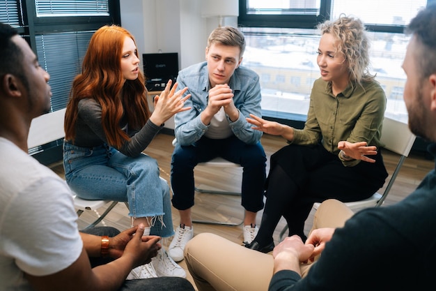 Friendly multiethnic business team share ideas during brainstorming on background of window. Young creative colleagues working together in teamwork discuss project plan in office.