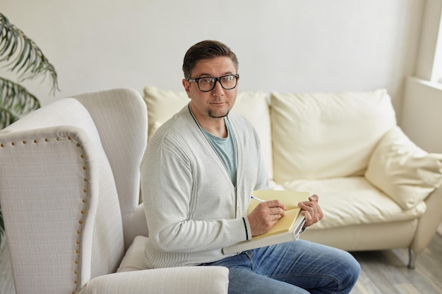 Friendly psychologist with clipboard leaning at wall in office empty space