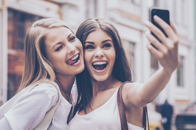 Friendly selfie. Two beautiful young women making selfie and grimacing