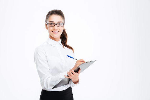 Friendly young smiling businesswoman with clipboard and pen over white wall