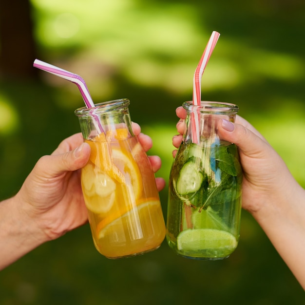 Friends celebrate with detox juice cocktails on green nature background