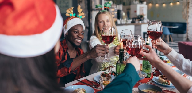 Friends celebrating Christmas eve clink glasses sitting at the table.