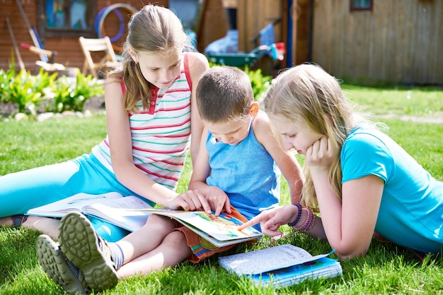 Friends children reading book outdoori on grass