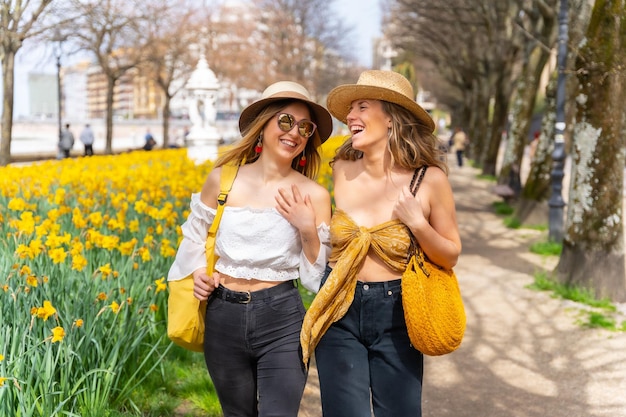 Friends in the city with straw hats walking next to some beautiful yellow flowers enjoying spring on vacation