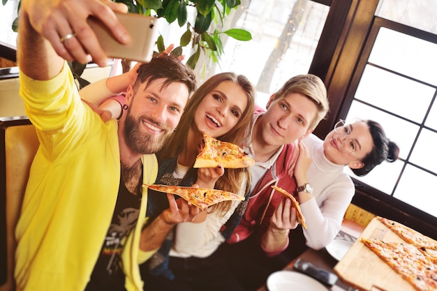  Friends eat pizza in a cafe, smile and shoot themselves on the camera smartphone