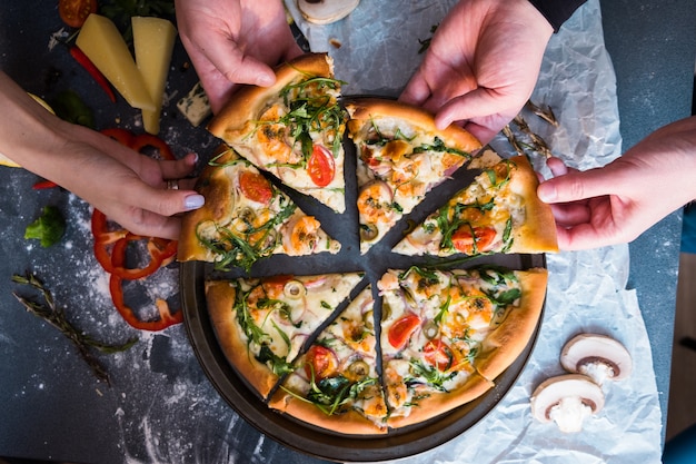 Friends eating pizza. People's hands grabbing a slice of pizza