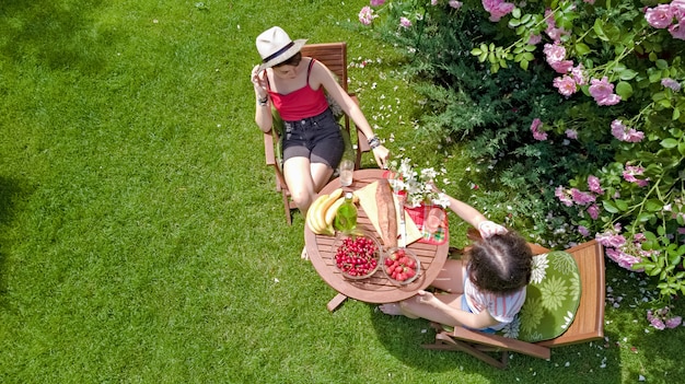 Friends eating together outdoors in summer garden, girls have picnic in park, aerial view of table with food and drinks from above