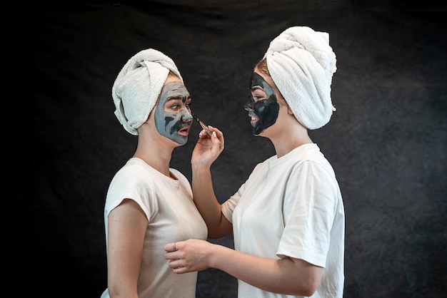 Friends female people make mud clay mask as anti aging treatment isolated on black Spa wellness Stay beautiful healthcare grooming