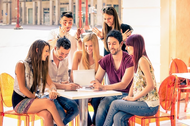 Friends group sitting at restaurant bar having fun with tablet pc Young students using portable computer in city center Connected people community Soft warm filter with focus in middle of frame