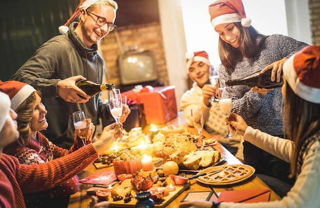 Friends group with santa hats celebrating Christmas with champagne and sweets food at home dinner