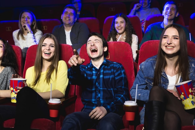 Friends of a guy and a girl are laughing loudly in a movie theater.