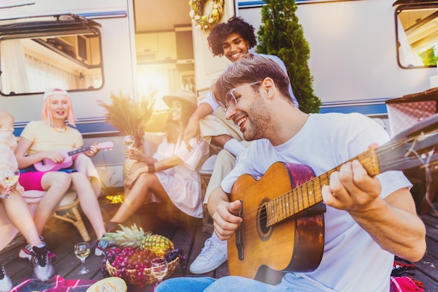 Friends have a picnic with a camper and play with guitar