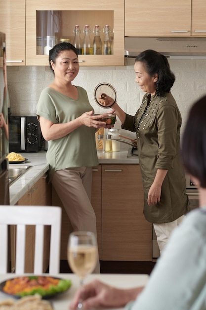 Friends helping senior woman to serve soup she cooked for dinner