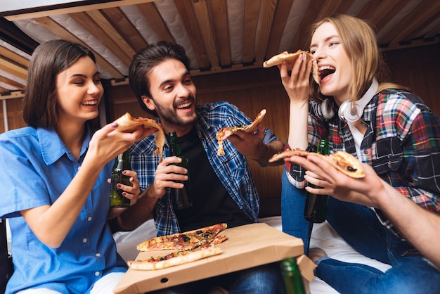 Friends laugh, hold pizza slices and eating.