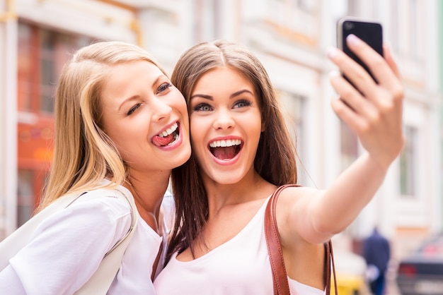 Friends making selfie. Two beautiful young women making selfie and grimacing