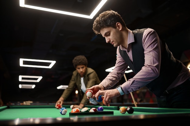 Friends playing billiard, young guy gathering ball