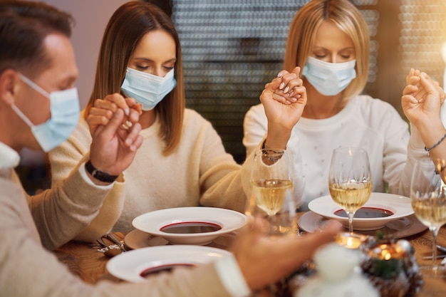 Friends praying before christmas dinner wearing mask. High quality photo