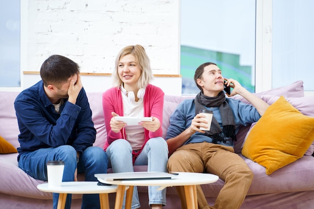 Friends sit on the couch chatting and using a smartphone desktop computer laptop