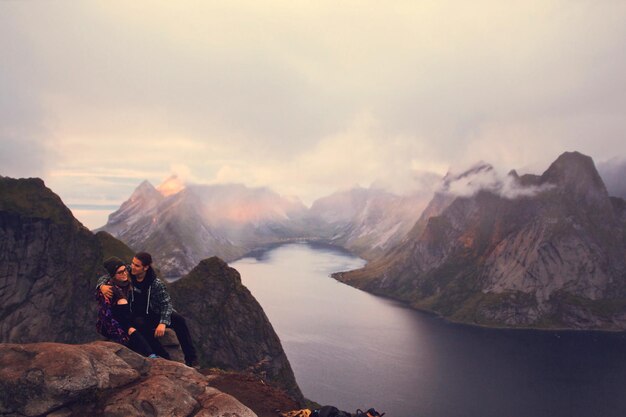 Photo friends sitting on mountain against sky during foggy weather