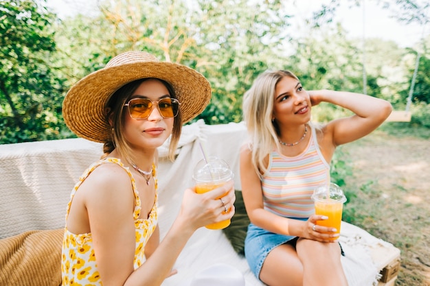 Friends sitting on a sofa in the backyard and drinking orange lemonade on summer sunny day.