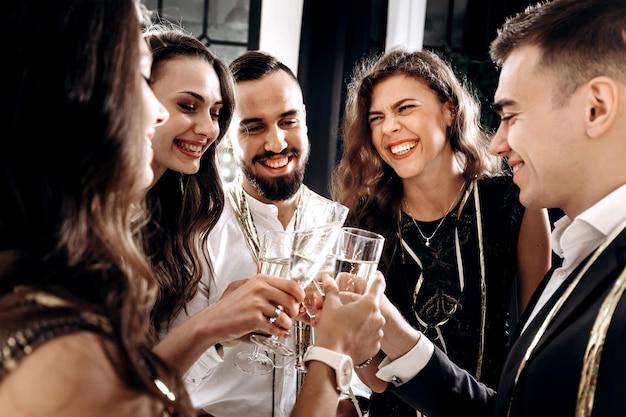 Friends in stylish elegant clothes smile together holding glasses of champagne in hands