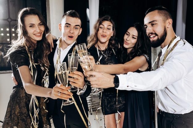 Friends in stylish elegant clothes smile together holding glasses of champagne in hands