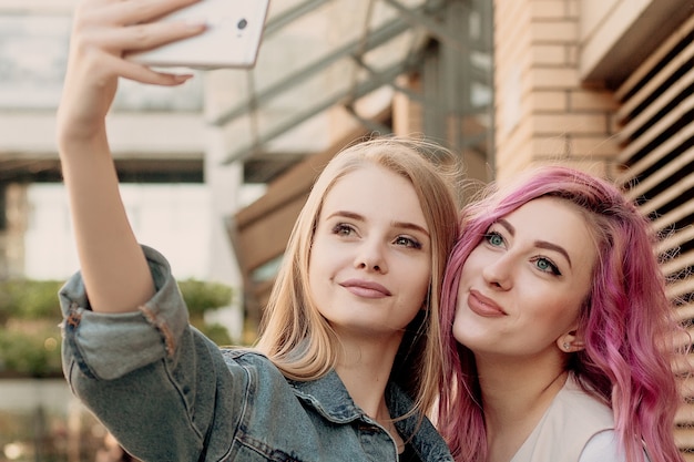 Friends taking selfie with a smart phone and making faces and fun. Closeup of girls making funny faces and smiling for selfie. Two happy girlfriends taking photo with their smartphone in the city