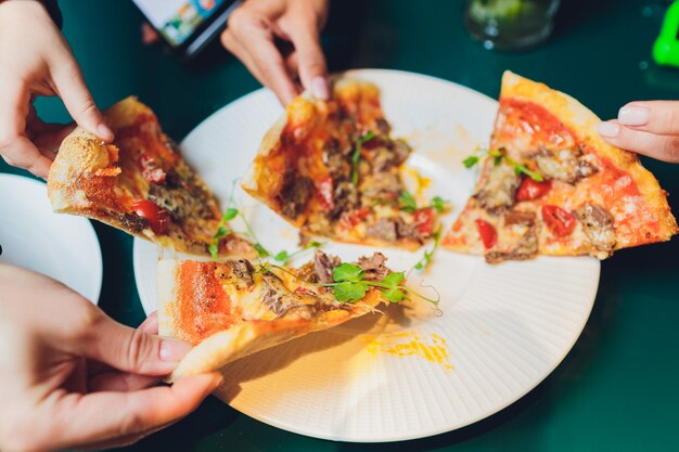 Friends taking slices of tasty pizza from plate, close up view.