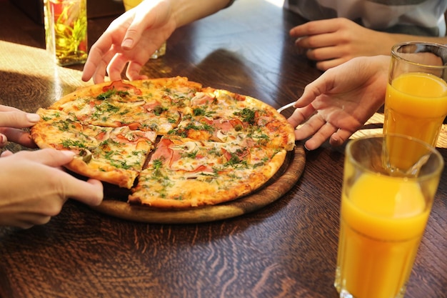 Friends taking slices of tasty pizza from plate close up view