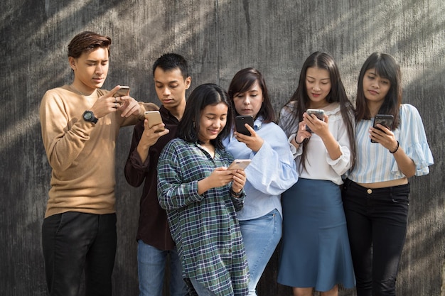 Friends using phones while standing against wall