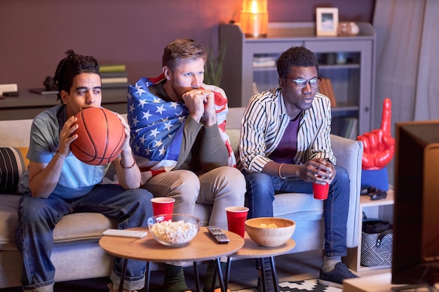 Friends watching football match at home lit by blue light