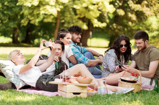 friends with smartphones on picnic at summer park