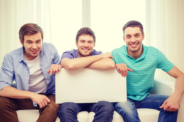 friendship and advertising concept - smiling male friends holding white blank board