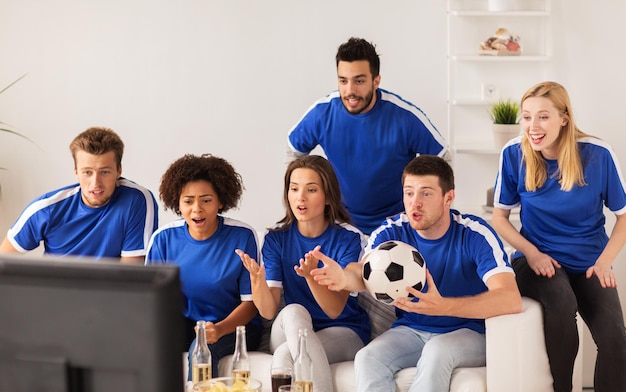 friendship, leisure, sport and entertainment concept - happy friends or football fans with ball watching soccer on tv at home