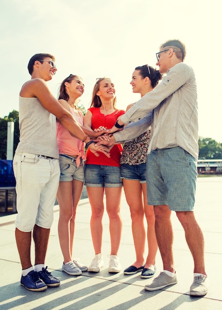 friendship, leisure, summer, gesturer and people concept - group of smiling friends with hands on top in city