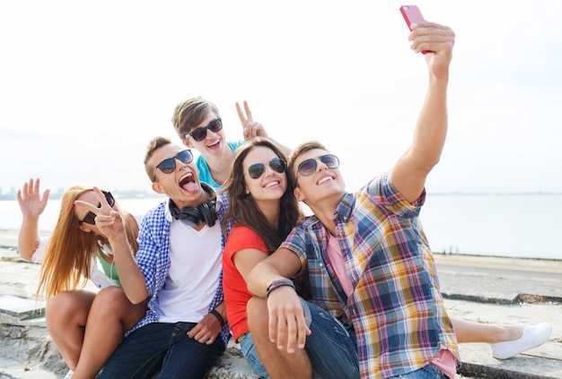 friendship, leisure, summer, technology and people concept - group of happy friends with smartphone taking selfie outdoors