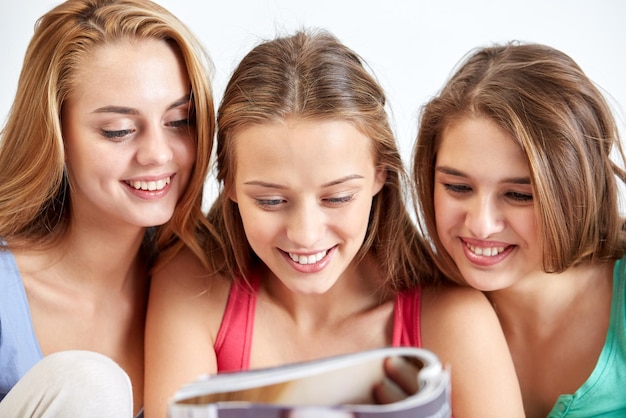 friendship, people and pajama party concept - happy friends or teenage girls reading magazine at home