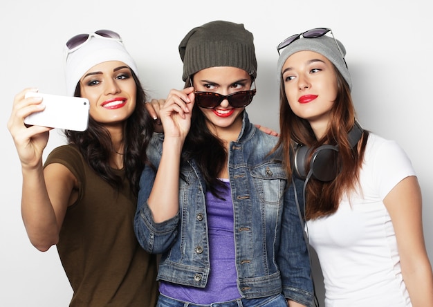 Friendship, people and technology concept - three happy teenage girls with smartphone taking selfie