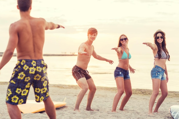 friendship, sea, summer vacation, water sport and people concept - group of smiling friends wearing swimwear and sunglasses with surfboards on beach