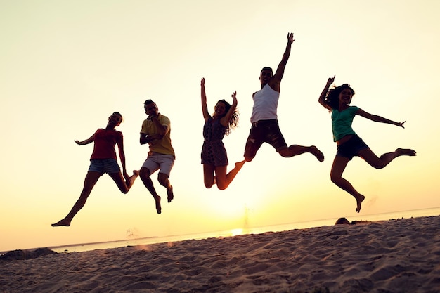 Photo friendship, summer vacation, holidays, party and people concept - group of smiling friends dancing and jumping on beach