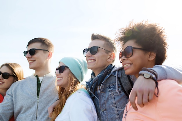 friendship, tourism, travel and people concept - group of happy teenage friends in sunglasses hugging outdoors